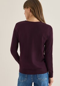 Bordeaux sweater met lange mouwen en een ronde hals, gemaakt van een zachte stof. Heeft ribgebreide boorden en een zoom. Draag met blauwe jeans.