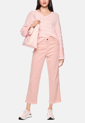 Frau trägt hellrosa gestrickten Pullover, kurze rosa Hose, passende rosa Sneakers und trägt eine weiche rosa Umhängetasche.