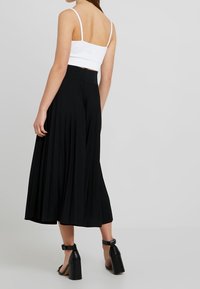 Svart plisserad midikjol med en flödande design, bärs med en figurnära vit cropped top och svarta blockklackskor.