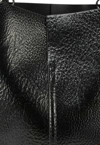 Zwarte leren tas met een gestructureerd, gekreukt oppervlak; beschikt over een uitgesproken naad in het midden; minimalistisch ontwerp, geen zichtbare hardware.