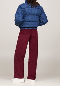 Niebieska puchowa kurtka z pikowanym wzorem i elastycznym paskiem w talii, zestawiona z bordowymi spodniami sztruksowymi i białymi trampkami.