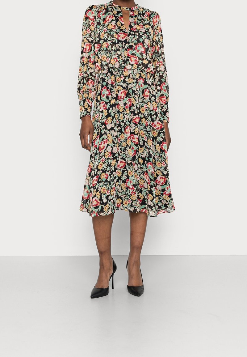 Robe midi fleurie en chiffon noir, avec manches longues, encolure en trou de serrure, et ourlet évasé orné d'un motif floral multicolore. Talons noirs élégants.