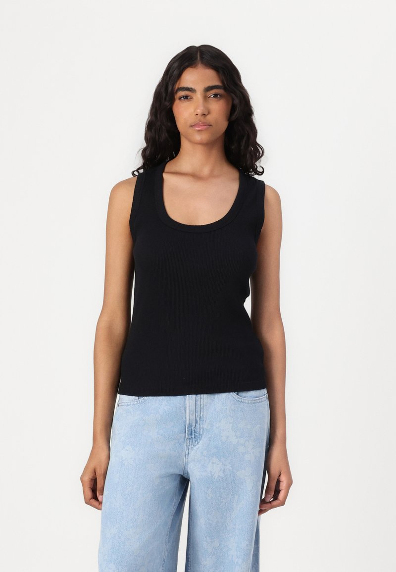 Svart ribbet tank topp med scoop hals, tettsittende design og skulderstropper, kombinert med lyseblå teksturerte vide jeans.