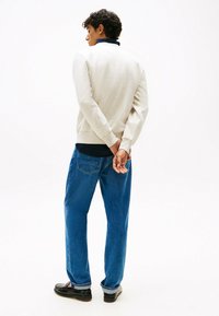 Felpa grigia chiara con colletto alto, abbinata a jeans blu scuro. I jeans hanno una vestibilità ampia e dettagli di cucitura visibili. Mocassini neri.