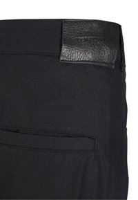 Zwarte broek met een gestructureerde leren patch op de taille. Heeft een achterzak met nette stiksels, een soepele stof en een aansluitend ontwerp.