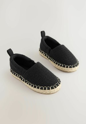 Črne slip-on čevlje iz teksturirane tkanine, z naravno jutenovo obrobo na podplatu, kontrastnim šivom in zadnjim trakom za enostavno obuvanje.