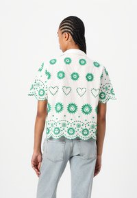 Wit kortgeleden shirt met groene bloem- en hartpatronen, een scalloped zoom en een knoopsluiting kraag, gemaakt van lichtgewicht stof.