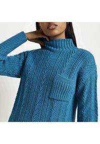 Maglione blu lavorato a maglia con colletto alto, caratterizzato da un motivo a zigzag testurizzato e una tasca applicata sul davanti. Cuffie a costine testurizzate.