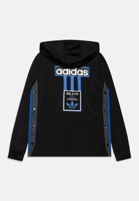 Svart huva jacka med blå ränder och grå detaljer. Har en stor vit "adidas"-logotyp och en grafisk patch med tre ränder. Tryckknappar på sidorna.