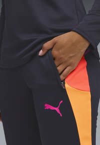 Spodenki sportowe Puma w kolorze granatowym z różowymi i pomarańczowymi siateczkowymi wstawkami, kieszenią na zamek oraz odważnym różowym logo. Miękki, elastyczny materiał zapewniający komfort.