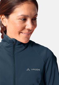 Giacca softshell blu navy con colletto alto, dotata di zip integrale e logo Vaude argentato. Texture liscia, design aderente e cuciture minime.
