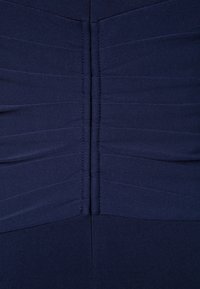Gros plan sur un tissu bleu marine avec une couture verticale et des plis horizontaux cousus créant des plis texturés.