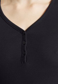 Black ribbed henley top featuring a V-neck and three button placket. The fabric is smooth and form-fitting with a textured appearance.