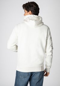 White hoodie with a hood, soft texture, featuring printed accents on the back and right sleeve. Paired with blue denim jeans.