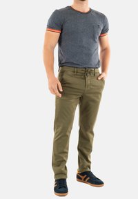 Camiseta gris de manga corta con puños a rayas naranjas, pantalones verde oliva con cordón y zapatillas azul marino con detalles naranjas.