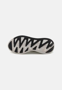 Svart og hvit sneaker såle med en teksturert gummioverflate, med et sikksakkmønster og formede detaljer for grep og stabilitet.