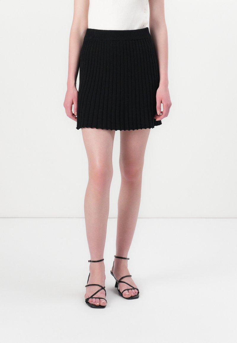 Jupe mini en tricot côtelé noir avec un ourlet en dentelle et une taille ajustée, associée à des sandales noires à lanières.