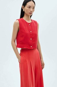 Rode mouwloze cropped top met een textuurfinish en drie knopen aan de voorkant; gecombineerd met lange rode geplooide broeken; minimalistisch ontwerp.