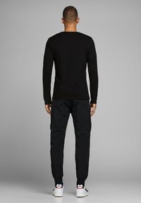 Camisa negra de manga larga, de ajuste relajado, combinada con pantalones cargo negros que cuentan con bolsillos laterales y puños elásticos. Zapatillas blancas con detalles.