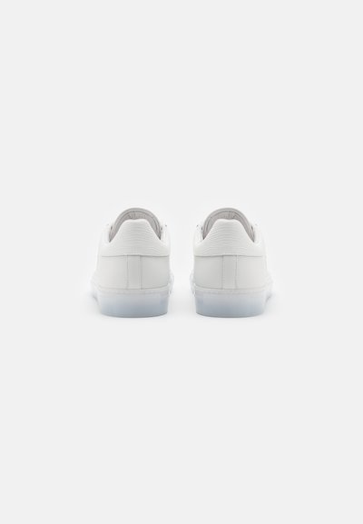 Zapatillas blancas con parte superior de cuero suave, textura estriada en el talón y suela de goma translúcida. Diseño minimalista sin acentos prominentes.