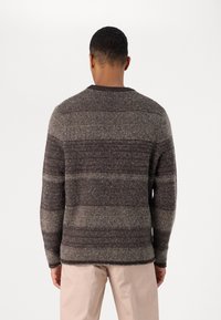 Pulover tricotat cu dungi gri închis și gri deschis, cu modele texturate și guler rotund, combinat cu pantaloni de culoare deschisă.
