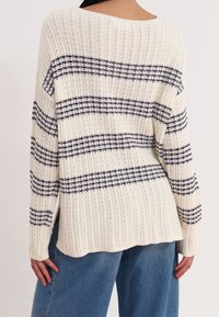 Maglione leggero color crema lavorato a maglia con righe blu navy, texture a coste, scollo ampio e spalle scese. Spacchi laterali all'orlo.