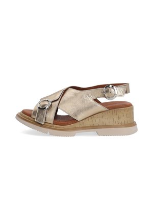 Sandale compensée en cuir doré avec bout ouvert, brides croisées, détails de boucle argentée, et semelle texturée beige avec semelle extérieure blanche.