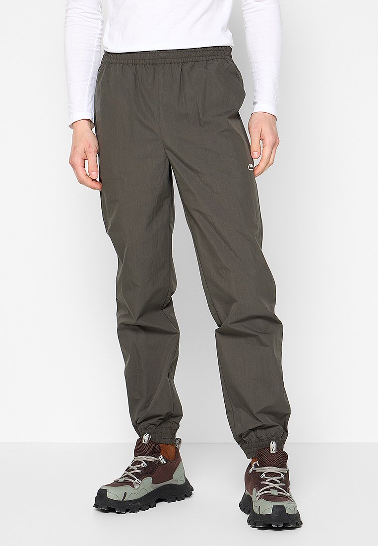 Herrenwindbreaker in Olivgrün, aus leichtem Material, mit elastischem Bund, gerafften Knöcheln, kombiniert mit robusten Wanderschuhen.