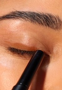 Eyeliner noir appliqué sur une paupière fermée avec de fines cils. La peau semble lisse, avec une teinte chaude et des détails de texture subtils.