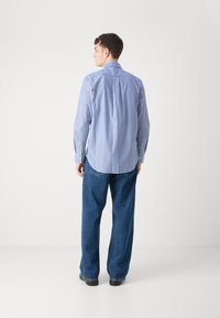 Striped blue and white long-sleeve shirt with a pointed collar, paired with loose-fitting blue denim jeans and black shoes.