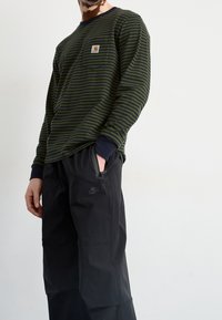 Zelená a námořnická pruhovaná košile s dlouhým rukávem a logem na kapsičce, spárovaná s černými kalhotami Nike s kapsou na zip.