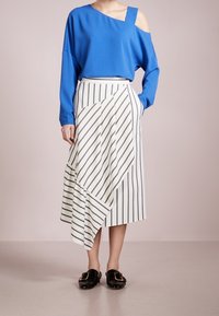 Blå off-shoulder top kombineret med en hvid nederdel med sorte diagonale striber. Nederdelen har en asymmetrisk kant. Sorte slip-on sko.