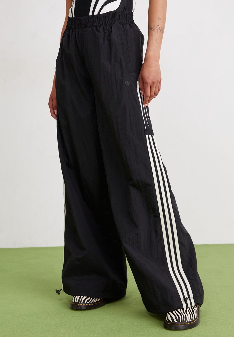 Pantalones de pierna ancha negros, confeccionados en un material ligero, con rayas verticales blancas a los lados y una cinturilla elástica, con un acabado texturizado.