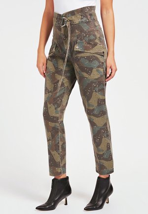 Pantalons avec imprimé camouflage dans des tons de vert, marron et bleu, dotés d'une taille ceinturée, de multiples poches et d'une coupe fuselée. Portés avec des bottines noires.