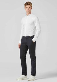 Chemise blanche à boutons, pantalon bleu marine, ceinture sombre avec des accents en métal et baskets blanches. Tissu lisse, coupe ajustée, couleurs neutres.