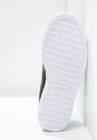 Baskets noires présentant une tige en cuir texturé et une semelle en caoutchouc blanche avec un motif géométrique. Comprend un logo sur le côté.