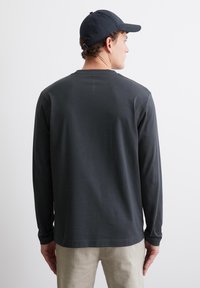 Donkergrijs shirt met lange mouwen en een ronde hals, heeft een gladde textuur en aansluitende mouwen; gecombineerd met lichte broeken.