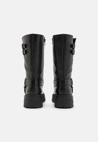 Botas de cuero negras hasta la rodilla con suela gruesa, doble hebilla lateral y cremallera interior para facilitar el uso. Textura suave y diseño resistente.