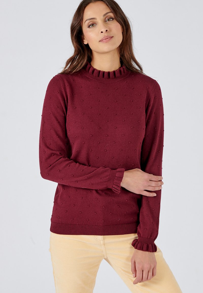 Maglione a maglia bordeaux con un motivo testurizzato, colletto alto a coste e maniche svasate. Il materiale sembra morbido e accogliente.