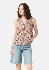 Blusa sin mangas floral en color crema con flores multicolor, con cierre de botones en la parte delantera y un corte relajado, combinada con pantalones cortos de mezclilla en un tono azul claro.