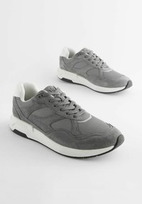 Grå sneakers med en blandning av mocka och mesh-material, en vit sula, rund tå och snörning med texturerade detaljer.