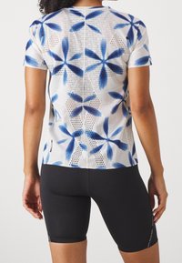 Short-sleeve athletic top in a floral blue and white mesh fabric; features a breathable design with cut-outs and a fitted silhouette.