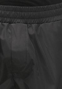 Fekete, fényes nejlon nadrág rugalmas derékpánttal és oldalzsebbel. A textúra sima, matt felületű, finom varrási részletekkel.