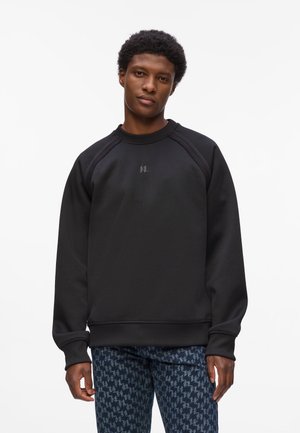 Sort sweatshirt med rund halsudskæring, tekstureret stof og raglanærmer. Har et diskret logo på brystet og ribstrikkede manchetter.