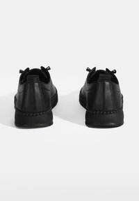 Des baskets noires avec une tige en cuir texturé, un bout arrondi et des détails tissés autour de la semelle. Talon renforcé et languettes pour un enfilage facile.