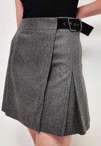 Grauer Wollmix-Rock mit einem schwarzen Gürtel, taillierter Passform und zwei vorderen Falten. Der Stoff hat eine feine Textur und ein dezentes Muster.