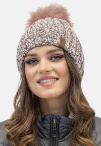 Knit beanie in beige and pink hues with a fluffy pink pom-pom on top, featuring a leather label on the front. Textured, warm design.