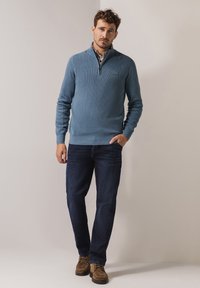 Light blue, zip-neck sweater made of a textured knit, paired with dark jeans and brown suede shoes. Simple, casual design with a fitted silhouette.