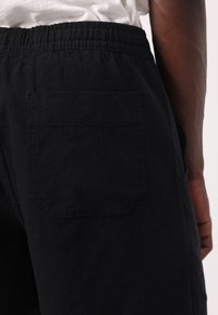 Schwarze Baumwollshorts mit einem elastischen Bund, ausgestattet mit einer einzelnen quadratischen Gesäßtasche und einem weichen, strukturierten Stoff.