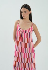 Różowa sukienka bez rękawów z pionowymi paskami w różnych odcieniach różu, czerwieni, fioletu i beżu. Miękka tkanina z płynącą sylwetką.